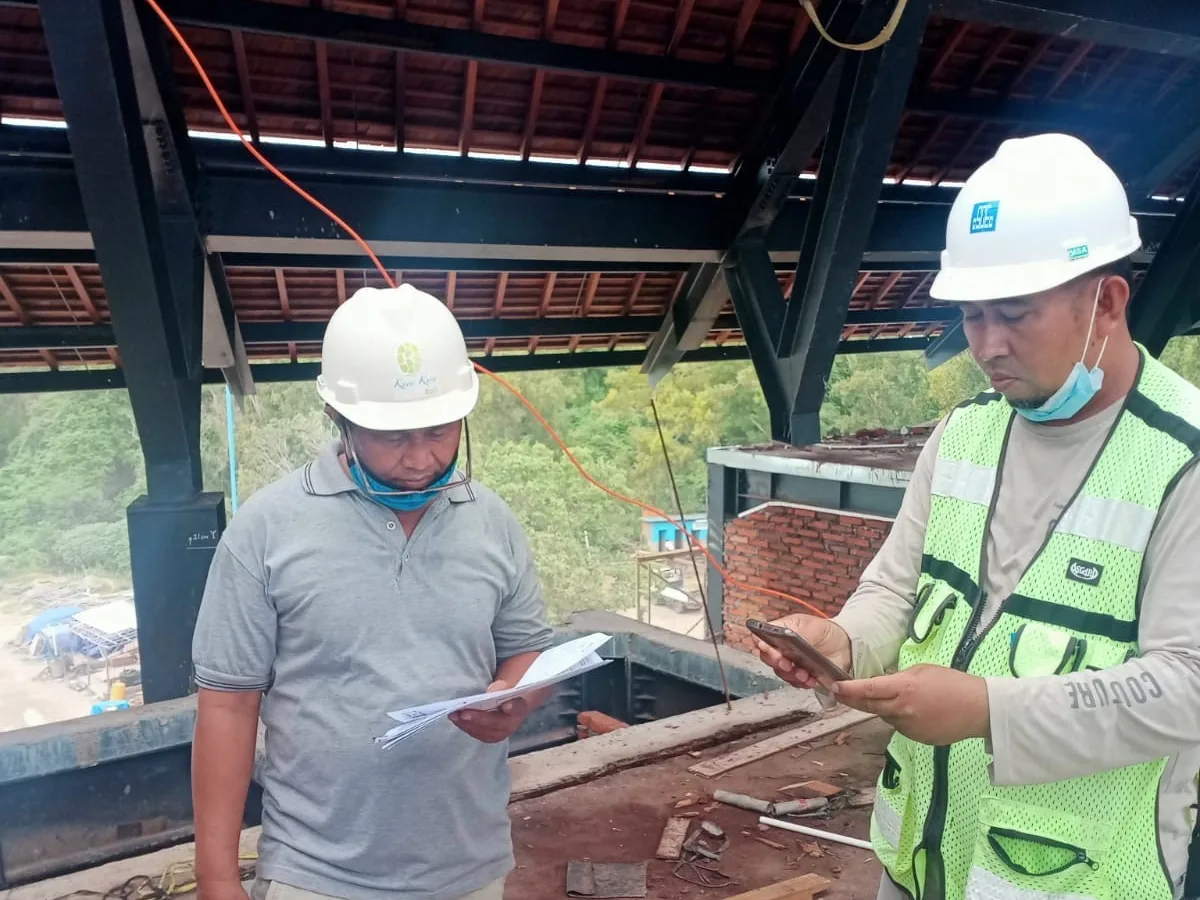 Dua pekerja berkoordinasi di area rangka atap